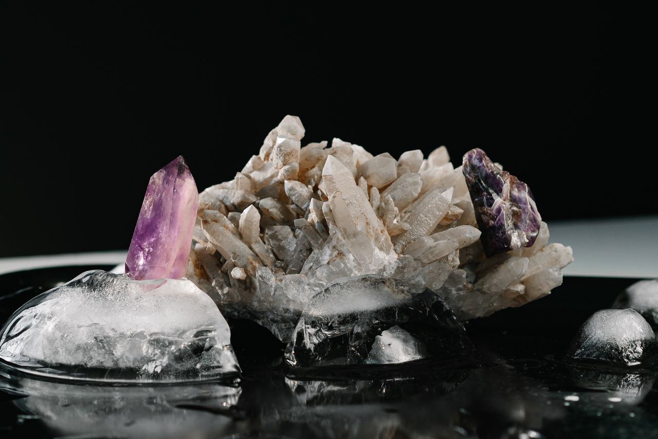 Amethyst and clear quartz crystals on ice with a black background, moody still life.